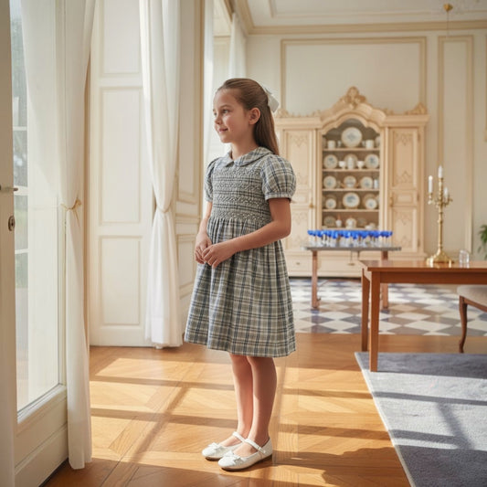 Young girl in a hand smocked dress standing in a well-furnished room with wooden floors and elegant decor.