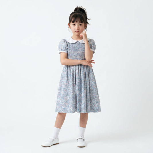 A young girl wearing a floral hand smocked dress with a white Peter Pan collar.