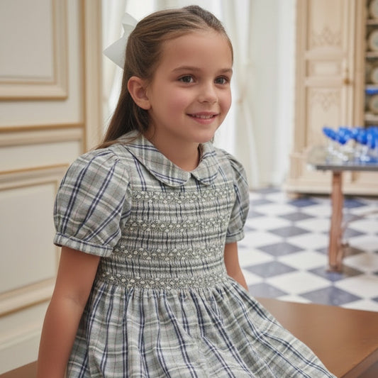 A young girl wearing a hand smocked plaid dress sitting in an elegant indoor setting.